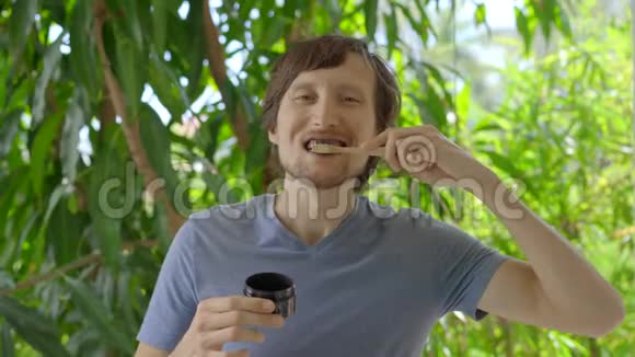 一个绿色环境中的年轻人用黑色活性炭粉刷牙用于牙齿美白他用的是视频的预览图