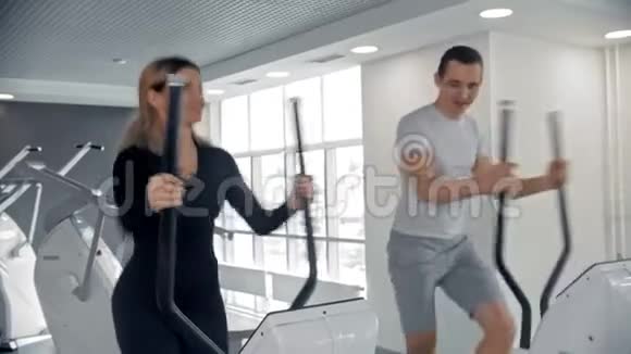 在室内的白色现代健身房里男人和女人用运动自行车训练他们的腿视频的预览图