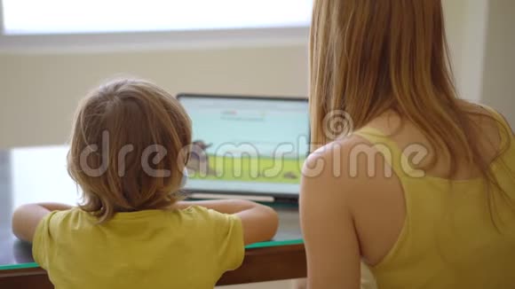 一位年轻的女士和她的小儿子在隔离期间坐在家里并在互联网学校使用平板电脑学习科罗纳视频的预览图