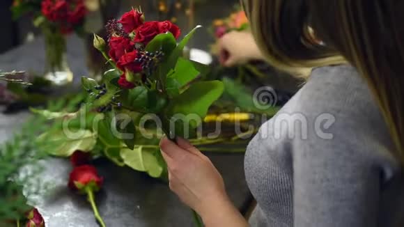 一个漂亮的女孩在她的工作室里收集一束深色的勃艮第红玫瑰男花匠创造了美丽的花束视频的预览图