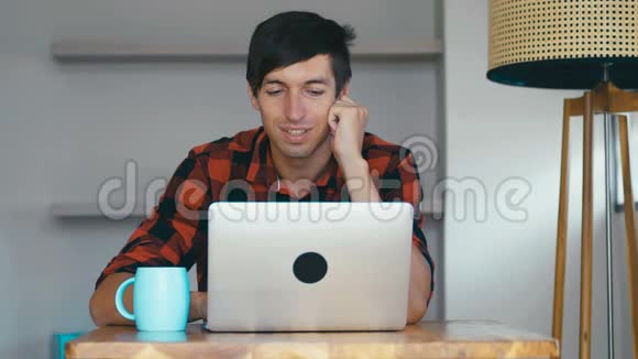 微笑英俊男子使用笔记本电脑的肖像自由职业者喜欢在家里用电脑工作和喝咖啡视频的预览图