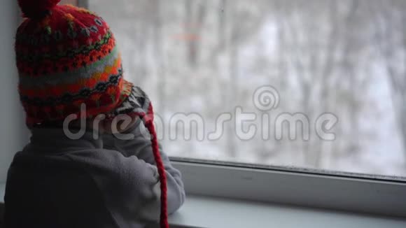 一个小男孩透过窗户看着一场大雪等待圣诞节的到来慢镜头视频的预览图