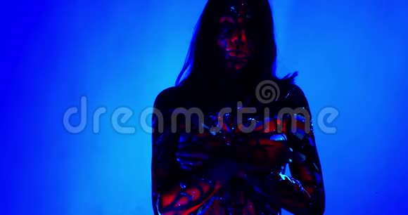 年轻女子在蓝色背景上摆姿势紫外线身体艺术4k视频的预览图