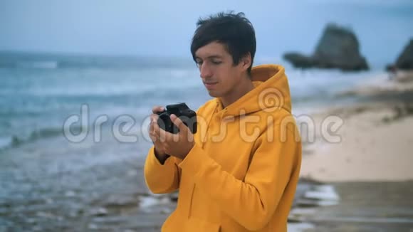 傍晚一位身穿黄色连帽衫的摄影师在美丽的热带海滩上拍照视频的预览图