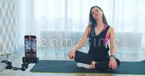 女人在电话里录瑜伽课在瑜伽垫上伸展四肢视频的预览图