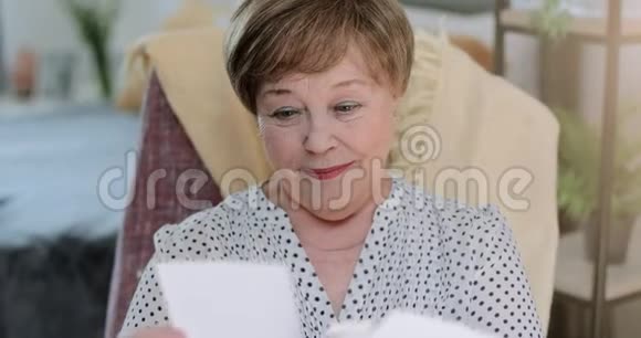 坐在椅子上时兴高采烈的祖母看着家庭照片好漂亮的退休女性视频的预览图