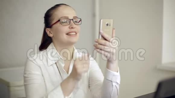 漂亮的生活方式女人手里拿着电话在办公室里视频的预览图