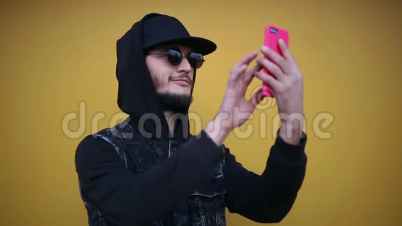 自信开朗的时髦女郎的肖像穿着全黑在智能手机上用粉红色的盒子做自拍照片视频的预览图