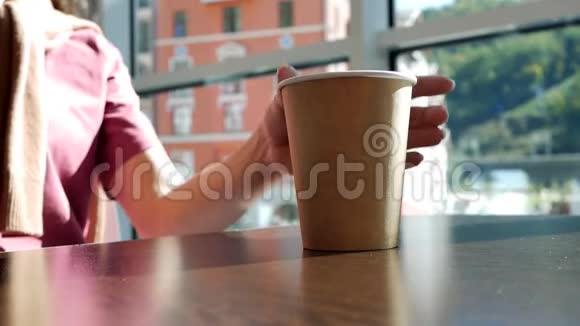 年轻女子从桌子上拿起咖啡馆里的纸杯茶喝茶把杯子放在桌子上视频的预览图