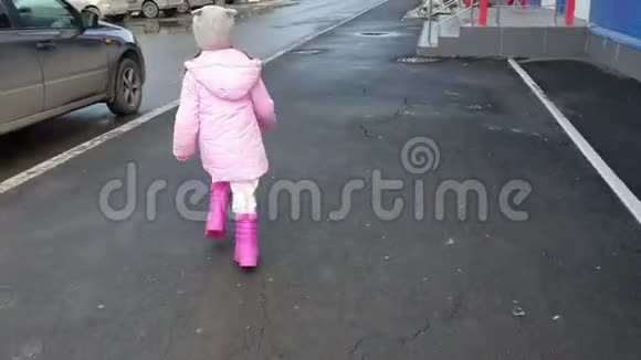 一个小女孩穿着粉红色的外套春天穿着橡胶靴沿着街道跑视频的预览图