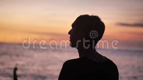 在海洋背景下欣赏美丽日落的年轻人的肖像剪影视频的预览图