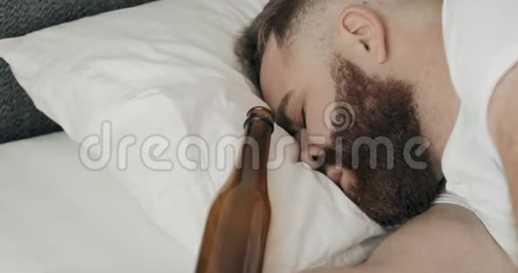 近距离观看年轻人宿醉和躺在床上枕头上的空瓶靠近他的头三十岁的家伙视频的预览图