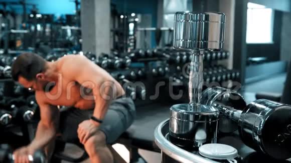 一位健美运动员坐在体育健身馆里抽着他的手肌肉视频的预览图