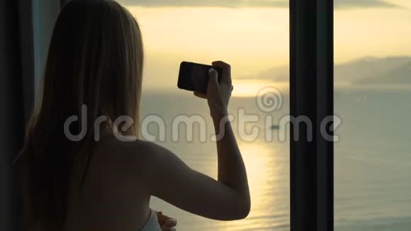 一位年轻女子在一间公寓里可以看到海岸和日出的全景她拍了一张美丽的日出照片视频的预览图