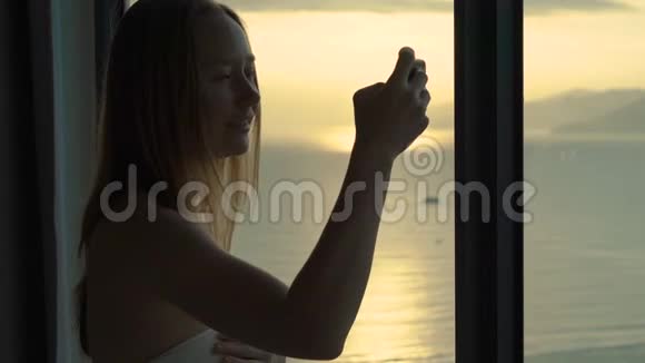 一位年轻女子在一间公寓里可以看到海岸和日出的全景她拍了一张美丽的日出照片视频的预览图