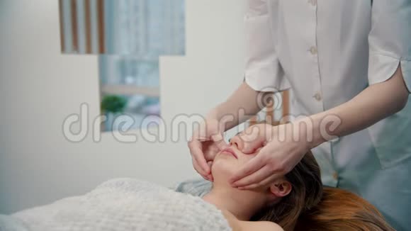 按摩按摩师在一位年轻女子脸上揉捏鼻唇褶皱视频的预览图