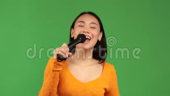 美丽开朗的亚洲女人快乐的享受卡拉OK麦克风在一个孤立的绿色背景视频的预览图