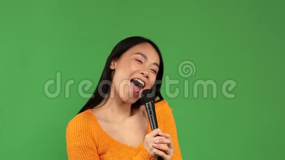 美丽开朗的亚洲女人快乐地享受卡拉OK麦克风在一个孤立的绿色背景视频的预览图