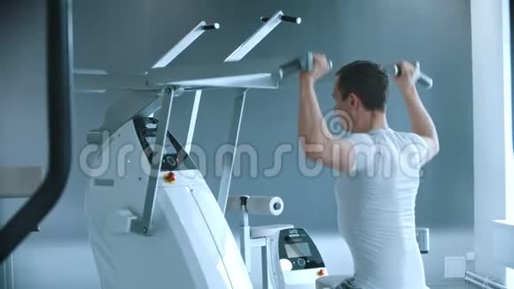 现代健身房一个男人坐在训练器械上在白色现代健身房训练他的手视频的预览图