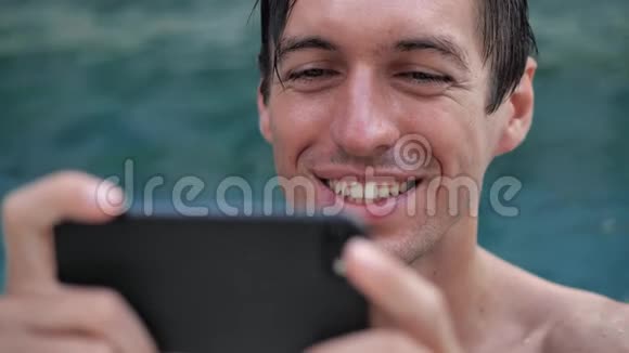 在游泳池里用智能手机观看视频的微笑年轻人特写视频的预览图