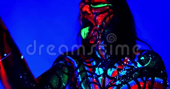 一位年轻女性的肖像有紫外线的身体艺术和发光的绿色舌头4K视频的预览图