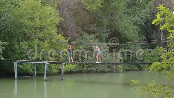 在河上的悬索桥上为摄影师摆了一个火红头发的迷人年轻女子视频的预览图