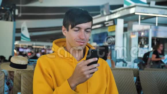 穿着黄色连帽衫的英俊的白种人坐在机场的候机室里等待航班在视频的预览图