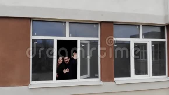 一对年轻的已婚夫妇在一栋新的公寓楼里愉快地从一扇开着的窗户问候视频的预览图