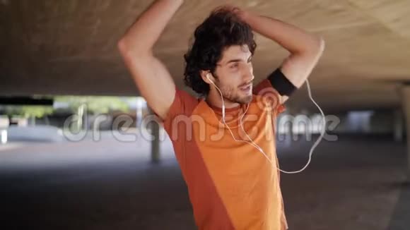 一位微笑的运动员的肖像年轻人在耳机上听音乐做伸展运动在下面热身视频的预览图