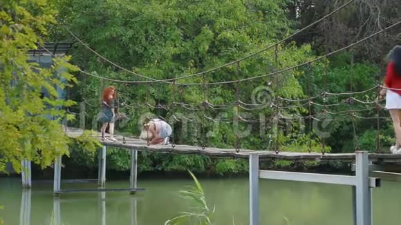 在河上的悬索桥上为摄影师摆了一个火红头发的迷人年轻女子视频的预览图