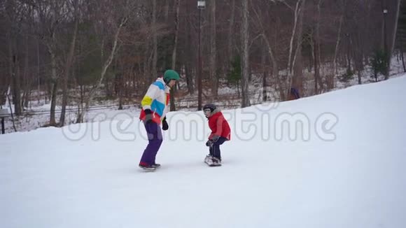 年轻人滑雪板教练教小男孩如何骑滑雪板冬季活动概念慢镜头视频的预览图