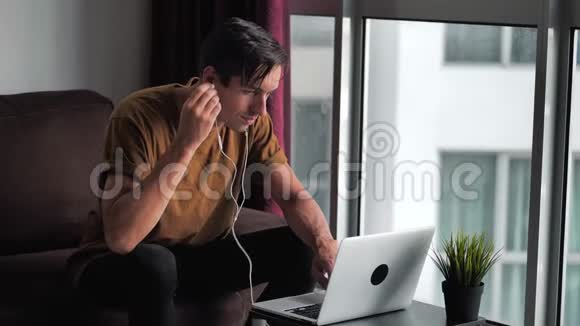 快乐的年轻人戴着耳机用笔记本电脑做电子商务上网购物看视频电影坐着视频的预览图