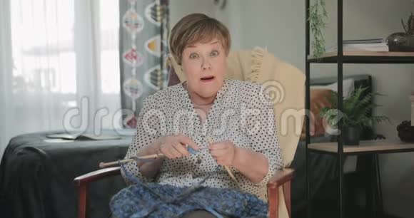 一位开朗的老太太坐在椅子上在她的公寓里编织前面的老年妇女看起来很惊讶视频的预览图