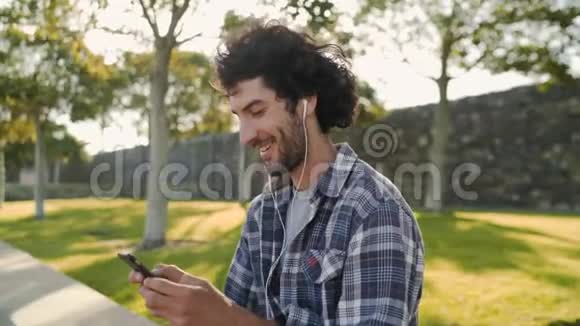 侧面观看一个快乐而放松的英俊年轻人在手机上通过耳机听音乐视频的预览图