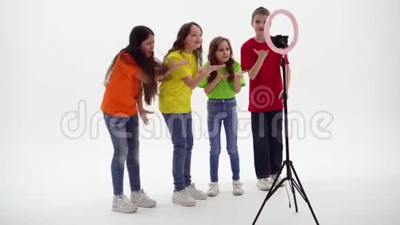 三个十几岁的女孩和一个男孩微笑着拍摄一段视频自拍手机安装在三脚架和环形灯上视频的预览图