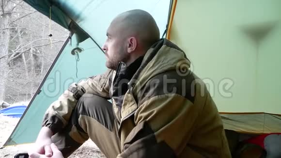 一个严肃的年轻人坐在野营帐篷里享受美丽的风景和思考徒步探险秋季运动之旅视频的预览图