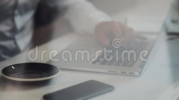 他在咖啡馆里用笔记本电脑工作年轻的自由职业者正坐在自助餐厅里桌上放着一杯咖啡打字或打字视频的预览图