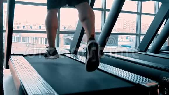 一个穿着运动鞋的男人在现代健身房的跑步机上跑步上面有全景窗视频的预览图