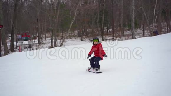 这个小男孩在滑雪板的第一课上摔倒了冬季活动概念慢镜头视频的预览图