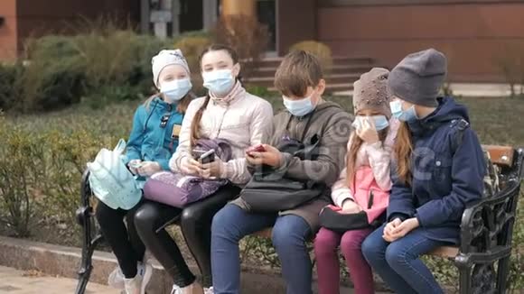 带医疗口罩的学龄儿童坐在长凳上视频的预览图