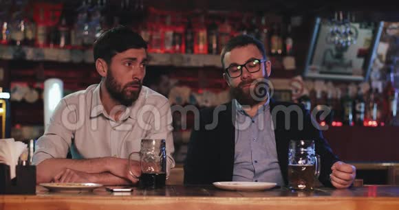 两个悲伤的朋友喝着啤酒在酒吧里聊天视频的预览图