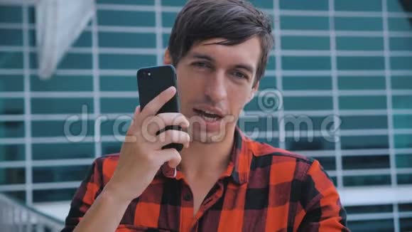年轻有魅力的人站在大现代办公楼附近在他的智能手机上说话男性接听电话视频的预览图
