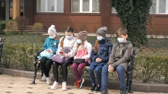 带医疗口罩的学龄儿童坐在长凳上视频的预览图