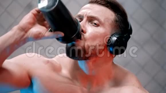 一个戴着耳机坐在长凳上喝着水的有魅力的拳击手看着镜头视频的预览图