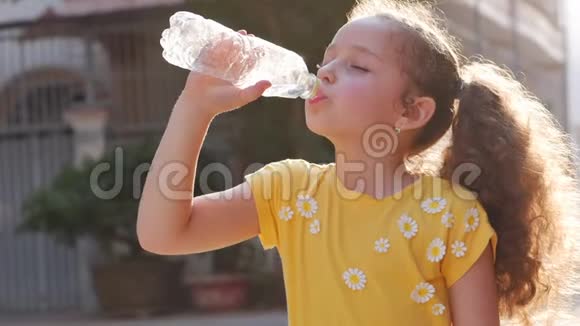 可爱的女孩解渴从房子附近的街道上的一个塑料瓶里喝慢动作小女孩急切地视频的预览图