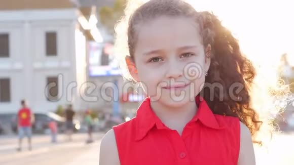 在一个阳光明媚的夏日滑稽的小女孩微笑着看着街上的摄像机快乐的脸上有一个学龄前儿童视频的预览图