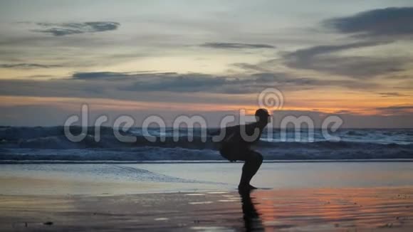 剪影运动员在日落时在海滩上练习锻炼运动员做后空翻和俯卧撑视频的预览图