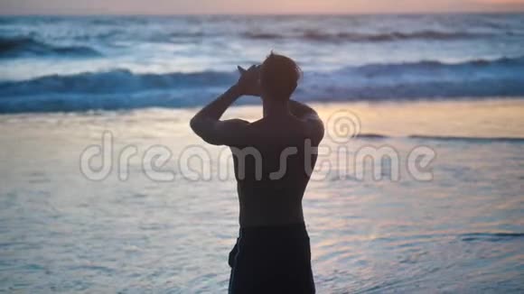 肌肉发达的男人抬起手的剪影背景是夕阳的大海视频的预览图