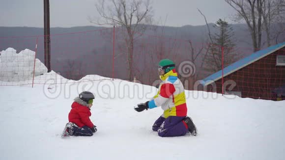 一个年轻人和他的小儿子在一个山区度假活动公园的滑雪坡上玩得很开心寒假概念视频的预览图