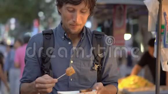 年轻人参观传统的韩国街头市场他正在竹签上吃鱼饼去韩国旅行视频的预览图